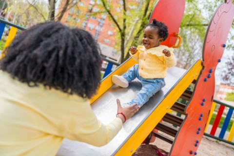 Happy african child playing with her mother in the slide in a public playground