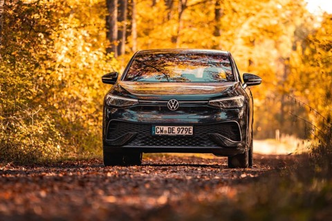 Car on forest road in autumn with colourful leaves and yellow light, electric car VW ID5,