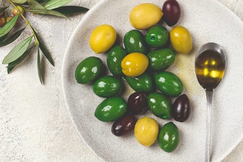 A mix of olives, a variety of Chalkidiki, verdi giganti and Kalamata, on a plate with a spoonful of