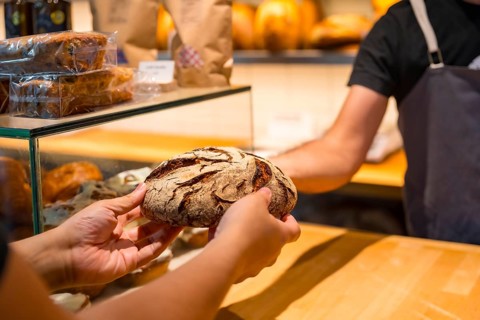 Customer hands in the bakery shop buying a loaf from the baker in the workshop workshop