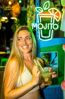 Vertical photo of a happy woman smiling while drinking mojito cocktail in a bar enjoying summer