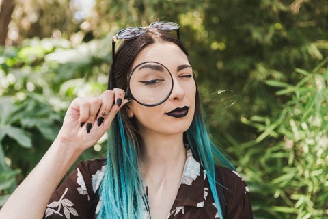 Young woman holding magnifying glass one eye