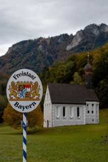 Free State of Bavaria sign with Nussdorf-Windshausen Kreuzkirche in the background, autumnal