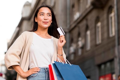 Happy woman outdoors holding shopping bags credit card