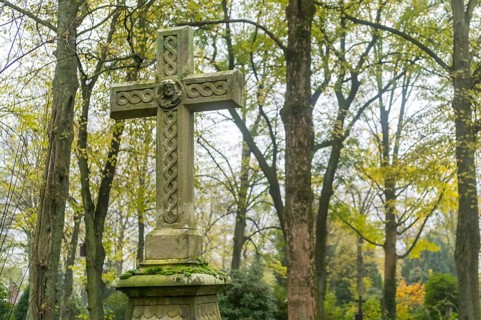 Old weathered celtic cross tombstone standing in a peaceful cemetery during fall