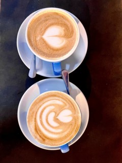 Top-down view of two cappuccinos with heart-shaped latte art, served in blue cups on a dark table.