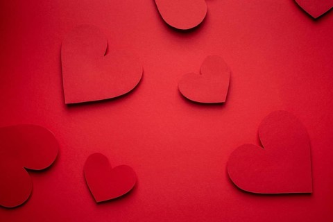 Red hearts cut from paper on red background, paper craft origami style, from above. Romantic