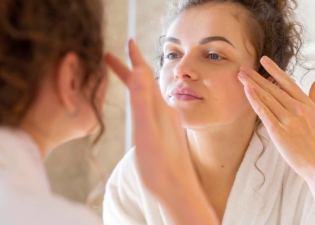 Woman applying cream face while looking mirror 2