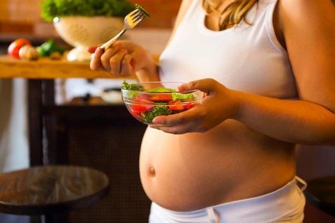 Young pregnant woman eating fresh vegetable salad at the kitchen. Pregnant nutrition