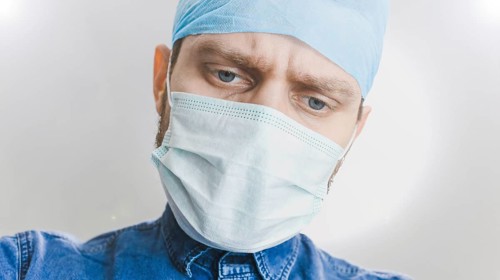A focused medical professional wearing a mask and surgical cap, looking down