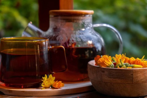 Calendula flower healthy tea in glass mug with tea pot on garden table. Herbal medicine Delicious