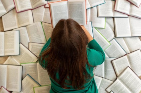 Top view of anonymous female student lying on books and reading during exam preparation