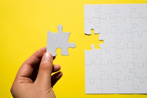 Person s hand holding missing white jigsaw puzzle piece yellow backdrop