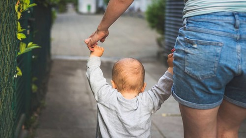 Learning to walk concept: Toddler is holding the hand of his mother, making his first steps. Close