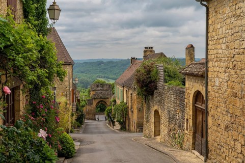 Domme, France - 12 May, 2022: picturesque street with stone houses and blossoming flowers in the