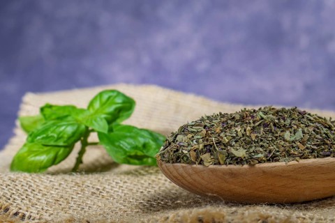 Dried basil ground in a wooden spoon with freshly cut basil leaves on a burlap cloth