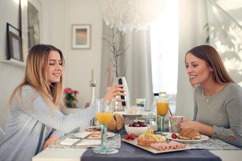 Smiling attractive young teenager showing her mother her mobile phone as they sit enjoying a