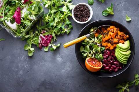Quinoa salad in bowl with avocado, sweet potato, beans, herbs, orange on concrete rustic background
