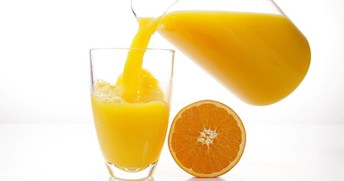 Orange Juice being poured into Glass against White Background