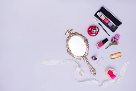 Vintage hand mirror lipstick nail varnish sponge perfume bottle eyeshadow palette purple background