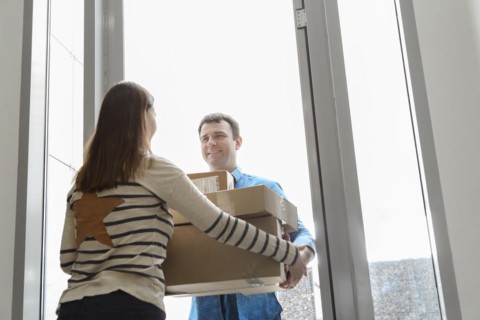 Fast and reliable service. Cheerful young courier giving a cardboard box to a young woman standing