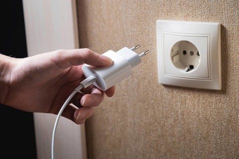 A young woman inserts a plug into a socket. A young woman plugs a charger or electrical appliance