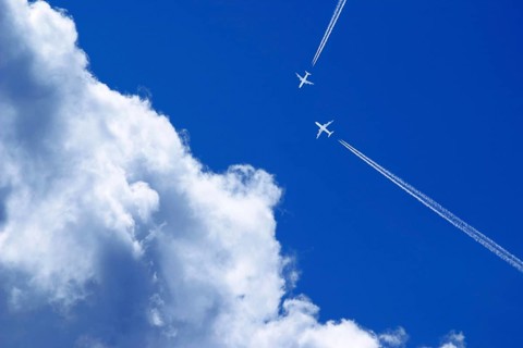 Two passenger airplanes with contrails on a collision course in the blue sky with clouds