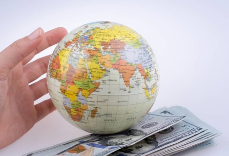 Human hand holding a model globe by the side of aAmerican dollar banknotes on white background