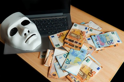 On a laptop there is a white mask and a pile of euro banknotes, cybercrime concept