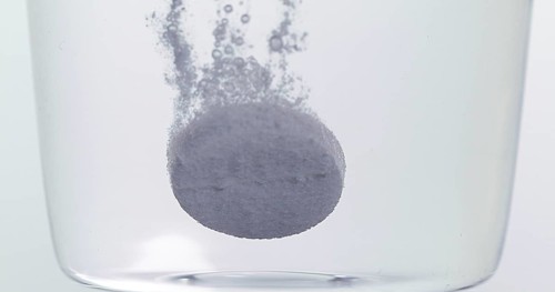 Tablets Falling and Dissolving into a Glass of Water against White Background