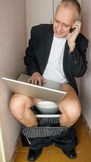 A workaholic adult businessman is using the computer laptop and the mobile phone, also called