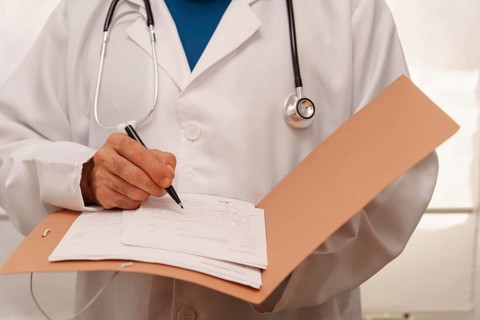 Unrecognizable doctor in white coat and stethoscope writing a prescription for a patient in his