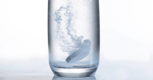 Tablets Falling and Dissolving into a Glass of Water against White Background