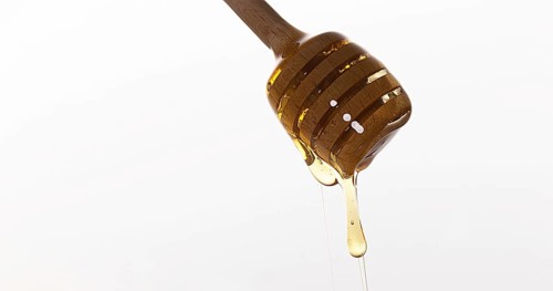 Honey Flowing from Spoon against White Background