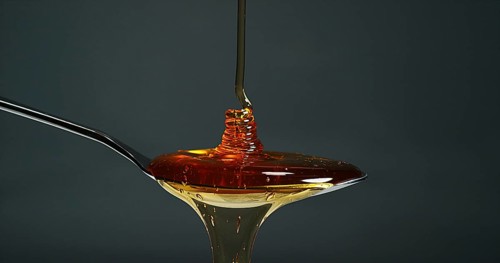 Honey Flowing in a spoon against Black Background