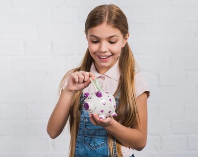 Smiling portrait girl inserting currency note white piggybank