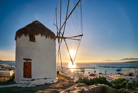 Romantic view of traditional Greek whitewashed windmill on hill. Chora town and harbor of Mykonos,