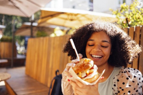 Young african american girl eating classic burger and drinking lemonade in the city. Outdoor woman