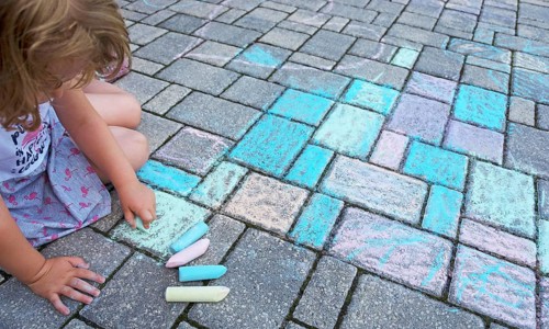 Child paints with colorful chalk on concrete pavement