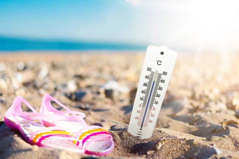 summer weather and hear concept, thermometer in sand at beach against sea and blue sky