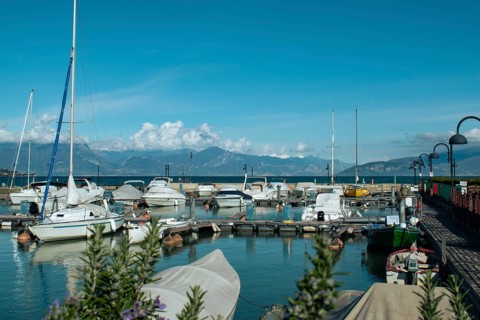 A harbour with numerous boats, mountains in the background and a clear sky, Sirmione, Lake Garda,