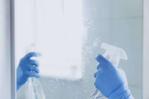 Cropped view of housekeeper woman hand in rubber blue gloves spraying chemical cleaner liquid to