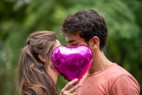 Couple kissing, covered by heart-shaped balloon