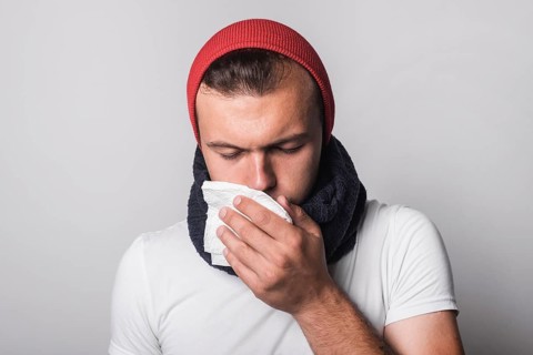 Young man suffering from cold flu against gray background