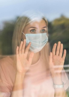 Front view woman with medical mask home touching window during pandemic