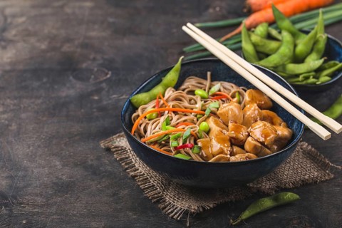Asian noodles with chicken, vegetables in bowl, rustic wooden background. Space for text. Soba