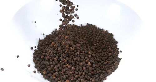 Black Peppercorns falling against White Background