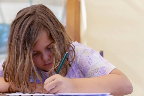 Close-up of a beautiful blonde girl in a colorful dress concentrating on school homework