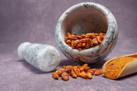 Whole cayenne pepper in a white marble mortar and ground cayenne pepper in a wooden spoon