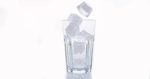 Ice Cubes Falling into Glass against White Background